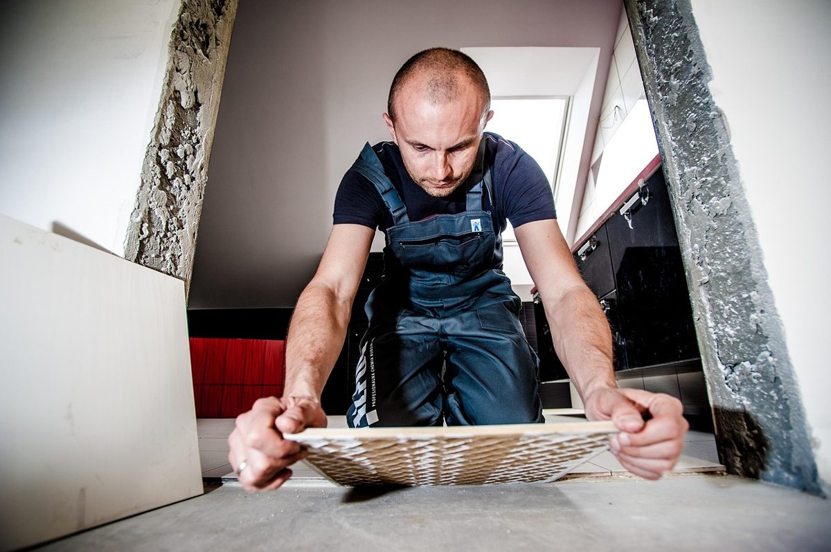 Installer laying tiles during the second-fix stage of a commercial washroom installation
