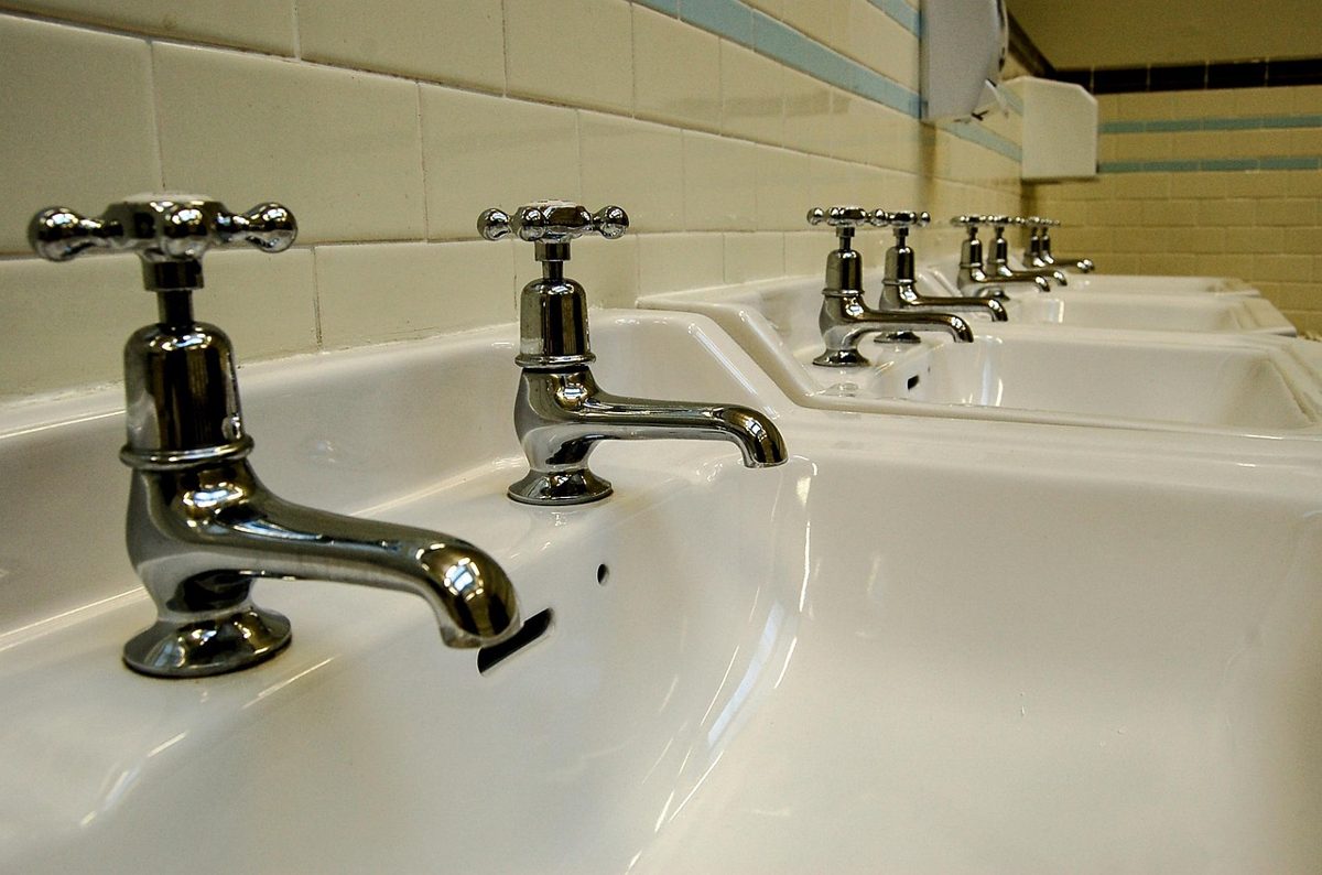 Row of washbasins and taps in a commercial washroom, kept stocked and serviced by washroom hygiene services